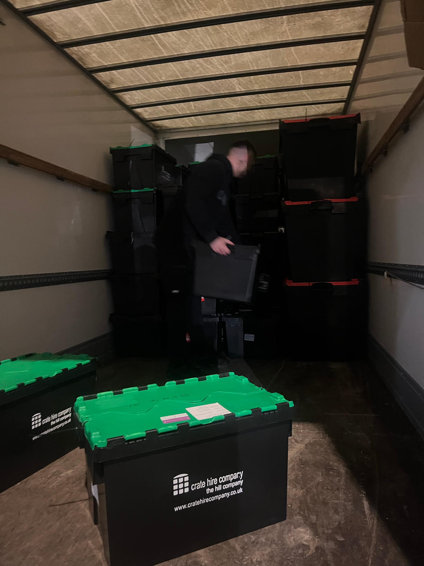 Mover loading stacked plastic crates inside a removals van